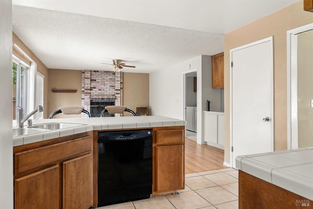 kitchen with light tile patterned flooring, black dishwasher, tile counters, ceiling fan, and a textured ceiling