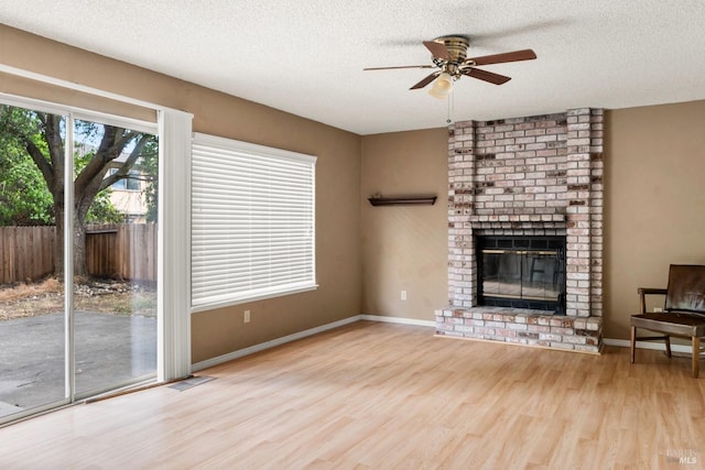 unfurnished living room featuring ceiling fan, a fireplace, a textured ceiling, and light wood-type flooring