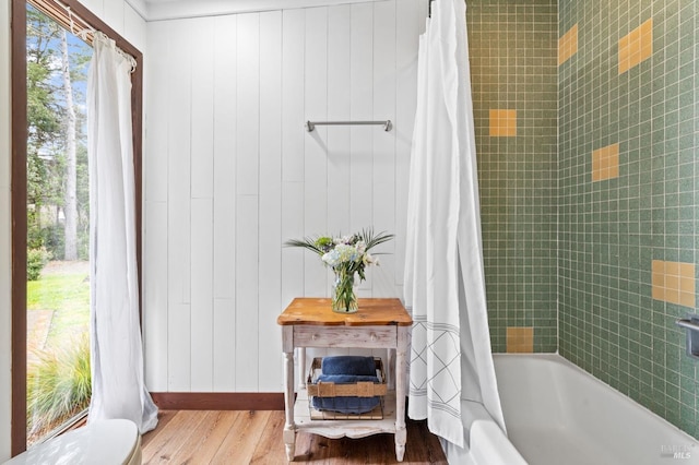 bathroom with toilet, hardwood / wood-style floors, wood walls, and shower / bath combo with shower curtain