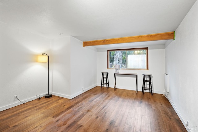 spare room featuring wood-type flooring and beamed ceiling