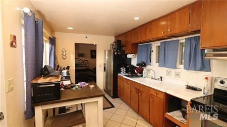 kitchen with range with electric stovetop, backsplash, stainless steel refrigerator, sink, and light tile flooring