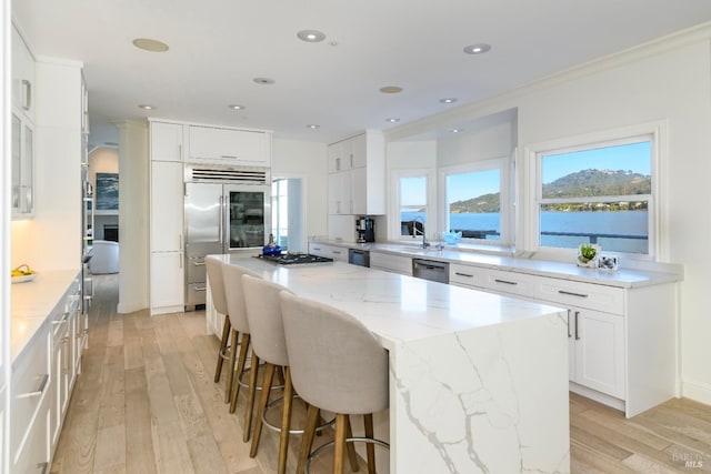 kitchen featuring white cabinets, appliances with stainless steel finishes, a kitchen island, a water view, and light stone counters