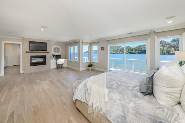 bedroom with light wood-type flooring, access to exterior, a fireplace, crown molding, and a water view