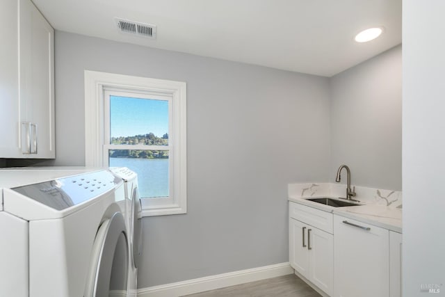 clothes washing area with cabinets, a water view, washing machine and clothes dryer, and sink