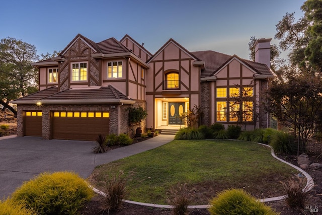 tudor home with stucco siding, a front lawn, concrete driveway, an attached garage, and a chimney