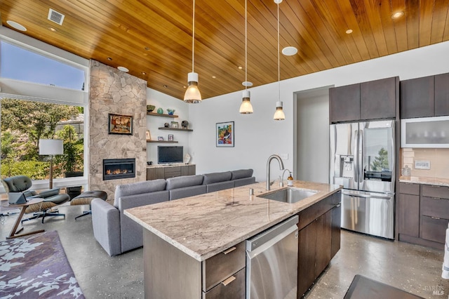 kitchen with dark brown cabinetry, sink, an island with sink, stainless steel appliances, and a fireplace