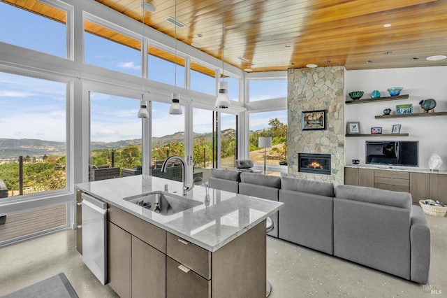 interior space featuring a stone fireplace, sink, light stone counters, a center island with sink, and dishwasher