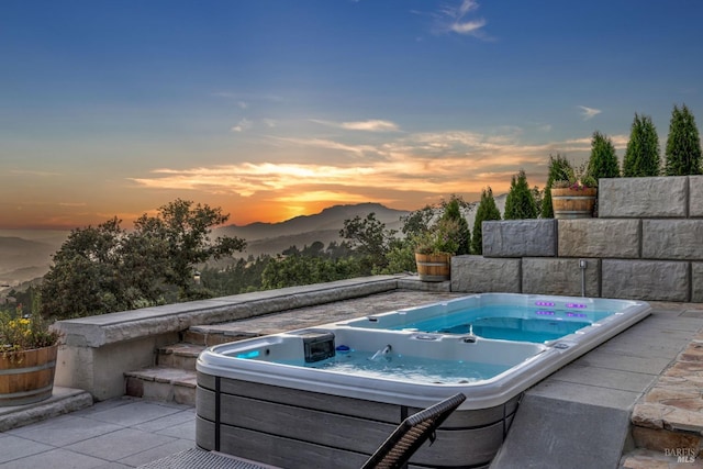 pool at dusk featuring an outdoor hot tub and a mountain view