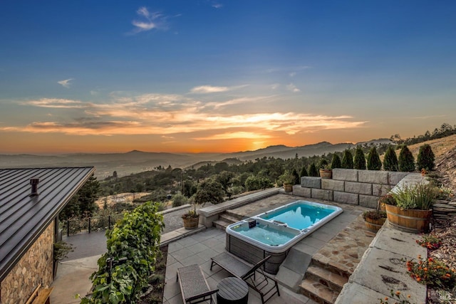 pool at dusk featuring an outdoor hot tub, a mountain view, and a patio area