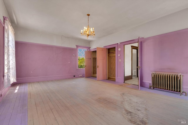 unfurnished room featuring hardwood / wood-style floors, an inviting chandelier, and radiator