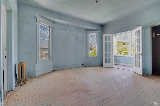 spare room with a wealth of natural light, light wood-type flooring, french doors, and radiator