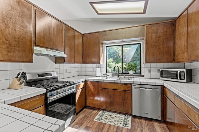 kitchen featuring tile countertops, lofted ceiling, sink, appliances with stainless steel finishes, and dark hardwood / wood-style flooring