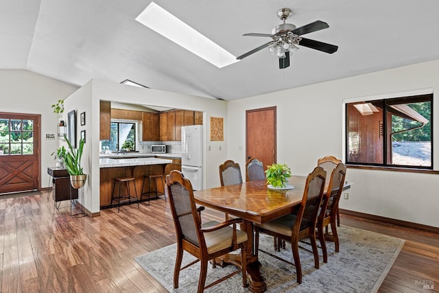 dining space with a wealth of natural light, lofted ceiling with skylight, ceiling fan, and dark hardwood / wood-style floors