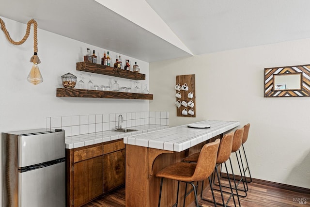 bar with tile counters, sink, dark hardwood / wood-style floors, stainless steel fridge, and lofted ceiling