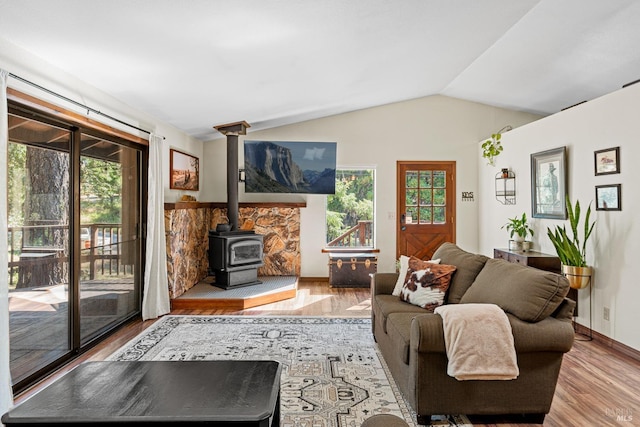 living room with a wood stove, light hardwood / wood-style flooring, and vaulted ceiling