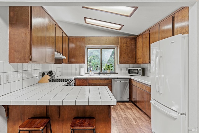 kitchen featuring sink, vaulted ceiling, light hardwood / wood-style floors, kitchen peninsula, and stainless steel appliances