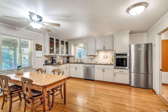 kitchen with sink, stainless steel appliances, ornamental molding, white cabinets, and light wood-type flooring