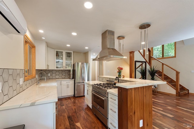 kitchen featuring sink, appliances with stainless steel finishes, island range hood, white cabinets, and decorative light fixtures