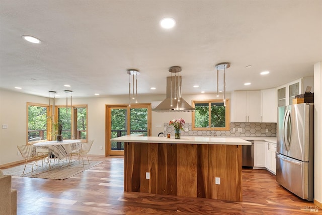 kitchen featuring appliances with stainless steel finishes, hanging light fixtures, island exhaust hood, white cabinets, and a kitchen island