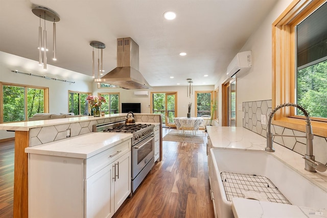 kitchen featuring island range hood, stainless steel stove, decorative light fixtures, white cabinetry, and sink