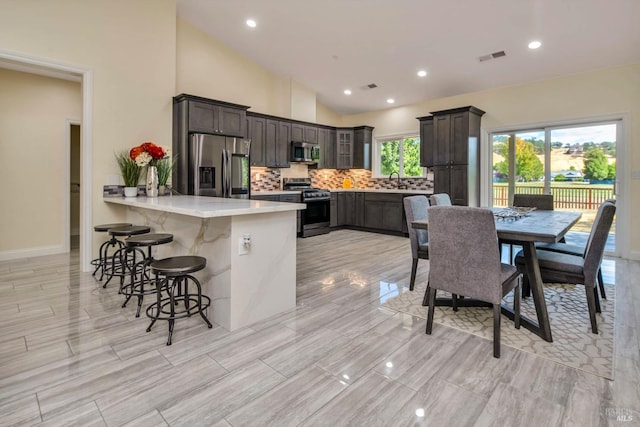 kitchen featuring lofted ceiling, kitchen peninsula, appliances with stainless steel finishes, dark brown cabinetry, and a breakfast bar area