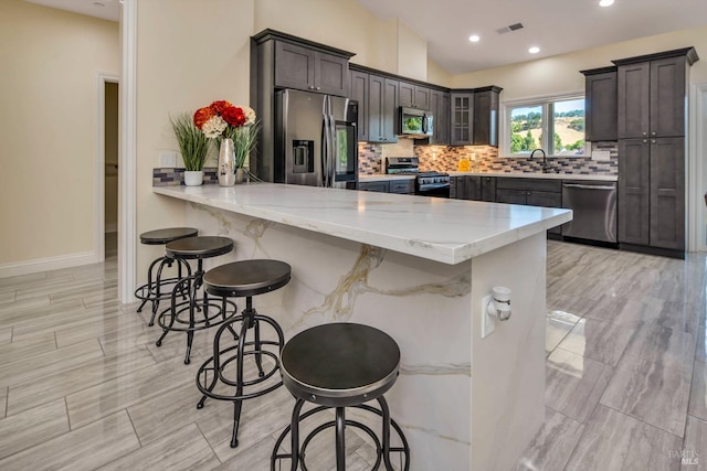 kitchen with stainless steel appliances, light stone counters, backsplash, kitchen peninsula, and a breakfast bar area