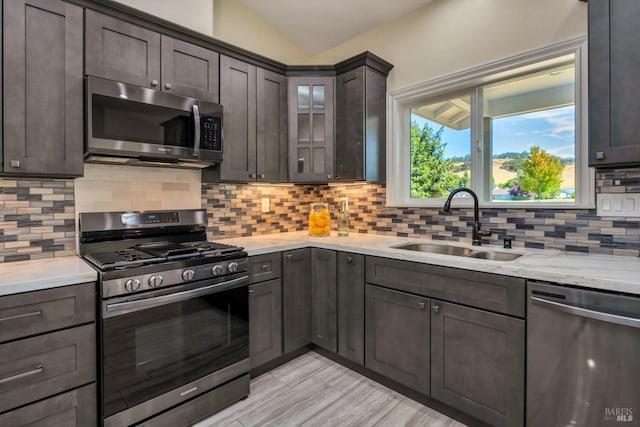 kitchen featuring decorative backsplash, dark brown cabinetry, stainless steel appliances, vaulted ceiling, and sink