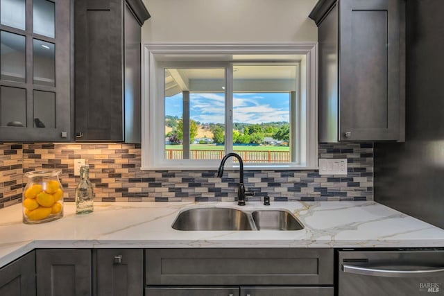 kitchen with light stone counters, tasteful backsplash, stainless steel dishwasher, and sink