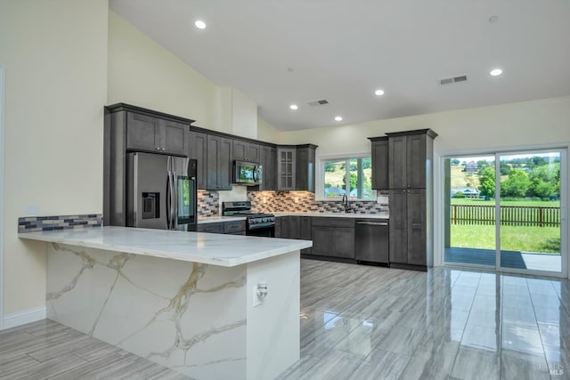 kitchen with backsplash, kitchen peninsula, vaulted ceiling, a breakfast bar area, and appliances with stainless steel finishes