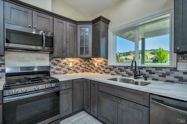 kitchen with sink, stainless steel appliances, light stone counters, vaulted ceiling, and decorative backsplash