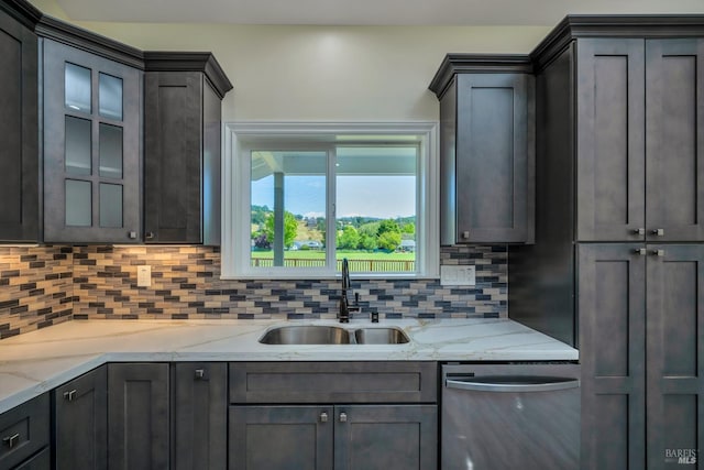 kitchen with stainless steel dishwasher, light stone counters, sink, and tasteful backsplash