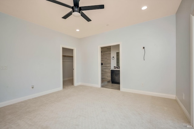 unfurnished bedroom featuring a walk in closet, light colored carpet, ceiling fan, and connected bathroom