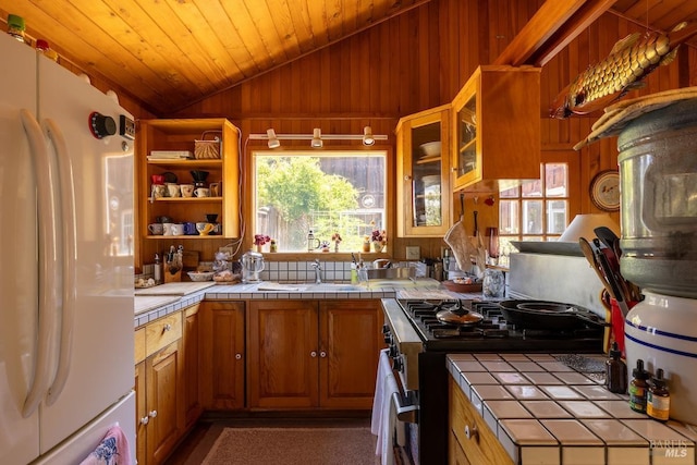 kitchen featuring plenty of natural light, vaulted ceiling, white refrigerator, tile counters, and stainless steel range with gas stovetop