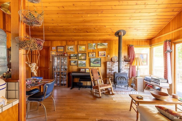 sitting room featuring hardwood / wood-style floors, wood walls, wooden ceiling, a wood stove, and vaulted ceiling