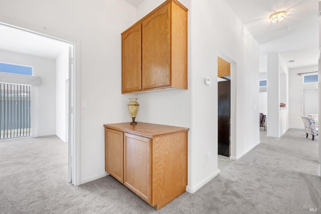 hall featuring baseboards, a wealth of natural light, and light colored carpet