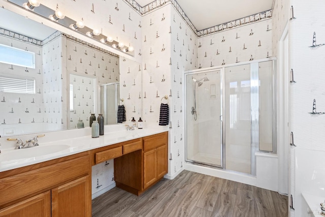 full bathroom with double vanity, wallpapered walls, wood finished floors, a shower stall, and a sink