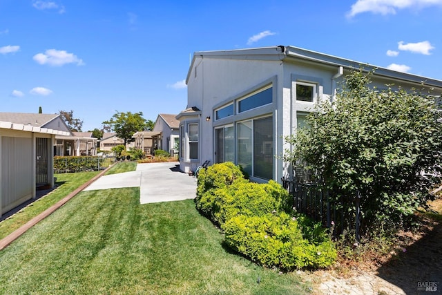 rear view of property featuring a patio area, a lawn, and stucco siding