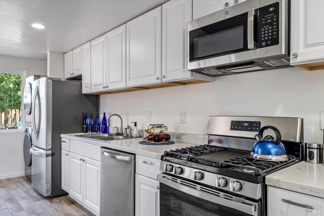 kitchen with sink, light stone counters, light hardwood / wood-style flooring, appliances with stainless steel finishes, and white cabinets