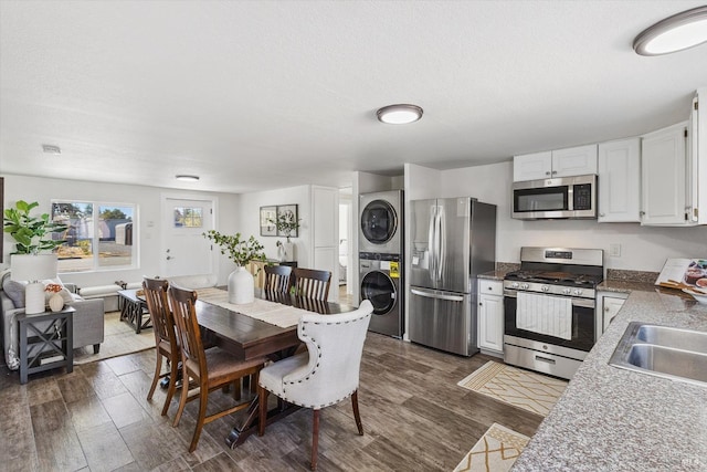 kitchen with stacked washer and clothes dryer, a textured ceiling, dark hardwood / wood-style floors, stainless steel appliances, and white cabinets