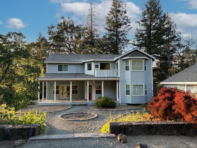 traditional home with a balcony, covered porch, driveway, french doors, and roof with shingles