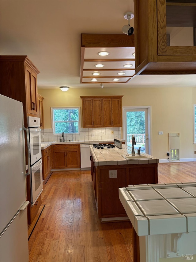 kitchen with decorative backsplash, white appliances, sink, tile counters, and light hardwood / wood-style flooring