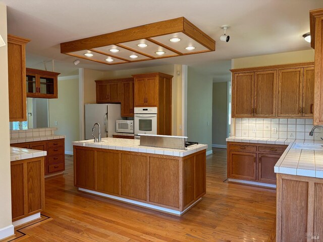 kitchen with light hardwood / wood-style flooring, white appliances, tasteful backsplash, a kitchen island with sink, and tile countertops