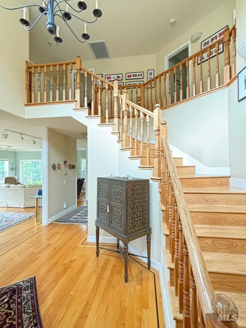 stairs featuring an inviting chandelier, wood finished floors, a towering ceiling, and baseboards