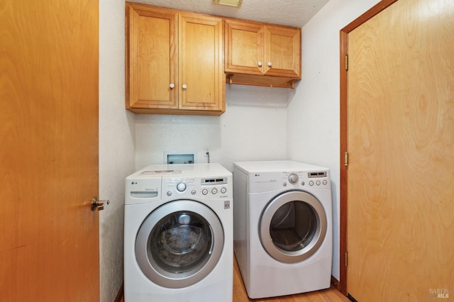 laundry area featuring a textured ceiling, cabinets, light wood-type flooring, and separate washer and dryer