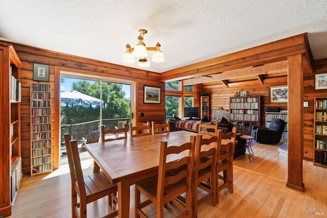 dining space with a textured ceiling, rustic walls, light hardwood / wood-style floors, and an inviting chandelier