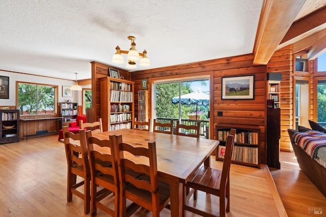 dining space featuring a chandelier, a textured ceiling, rustic walls, and light hardwood / wood-style floors