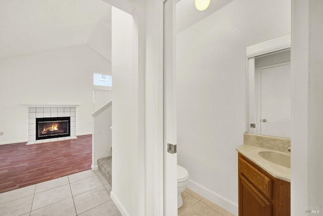 bathroom featuring vanity, a fireplace, hardwood / wood-style floors, toilet, and lofted ceiling