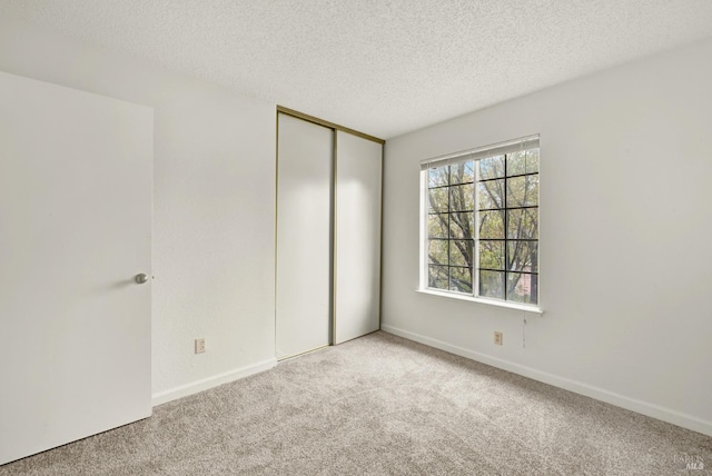 unfurnished bedroom featuring light colored carpet, a textured ceiling, and a closet