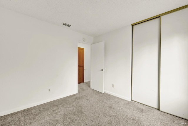 unfurnished bedroom featuring light colored carpet, a textured ceiling, and a closet