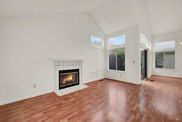 unfurnished living room featuring hardwood / wood-style floors, a tile fireplace, and high vaulted ceiling